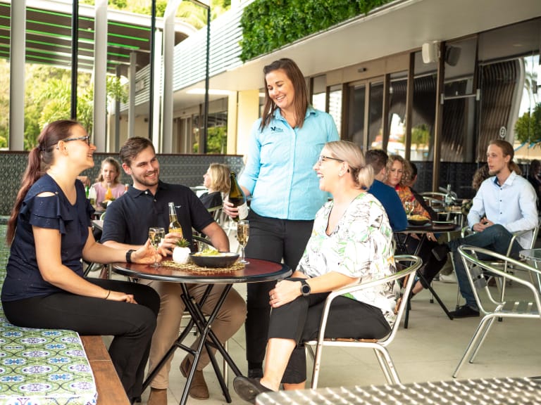 Person pouring wine to several people seated in an outdoor dining area