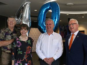 Three men and one woman smiling with a 40 balloon behind them